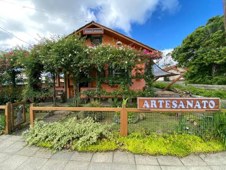 Casa laranja coberta de flores, com cerca de madeira e a placa "Artesanato" na frente