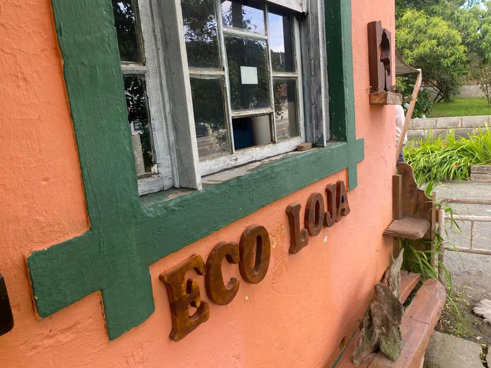 Parede laranja com o letreiro "Eco Loja" em letras de madeira, ao lado de uma janela verde