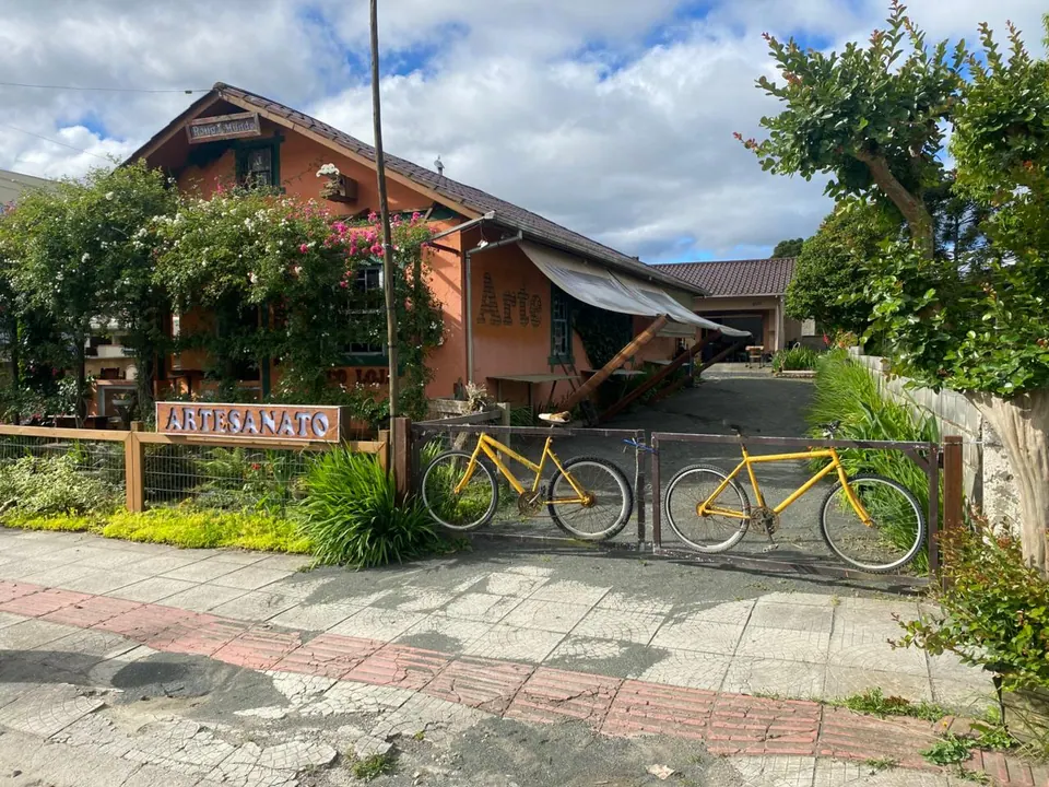 Fachada com a placa "Artesanato" e duas bicicletas amarelas presas ao portão