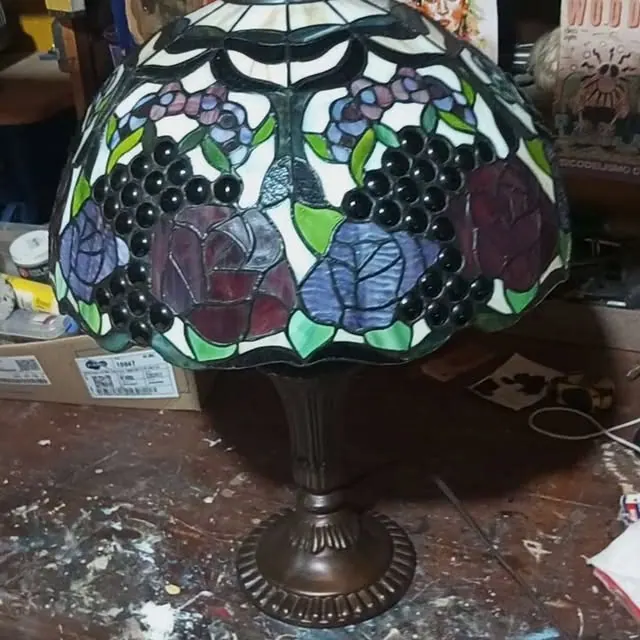 Lustre de vitral colorido, com rosas e uvas, restaurado sobre a bancada da oficina
