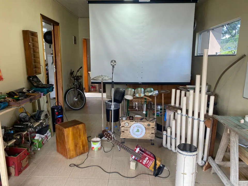Sala com instrumentos musicais feitos de materiais reaproveitados e uma tela de projeção
